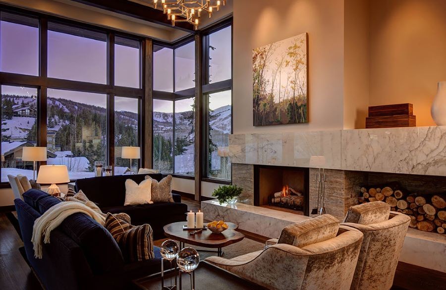 A living room with a lit fireplace and picture windows overlooking mountains.