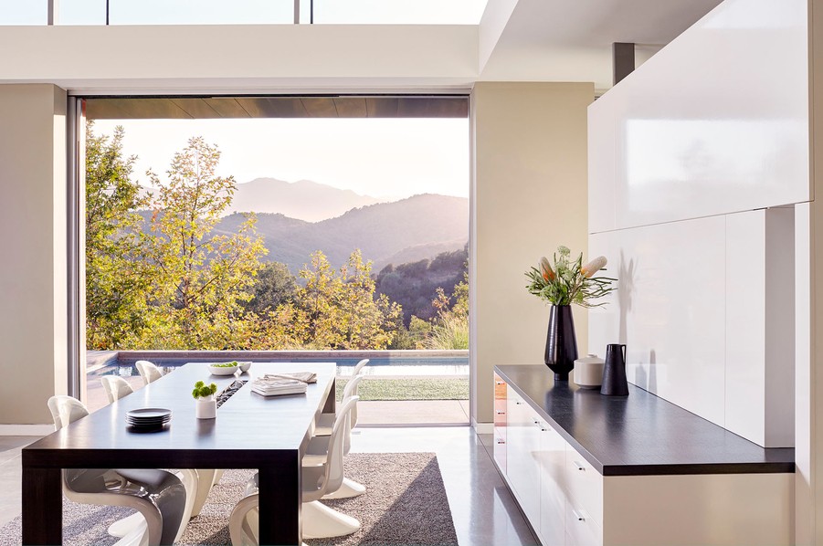 Minimalist dining area with retractable automated shades overlooking a mountainous landscape in a Boulder smart home. 